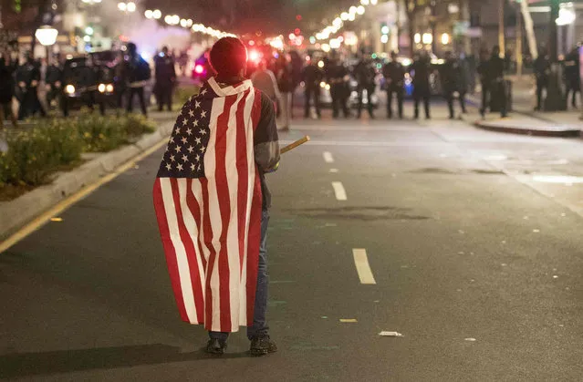A protester wearing an American flag faces police during an anti- Trump protest in Oakland, California on November 9, 2016 Thousands of protesters rallied across the United States expressing shock and anger over Donald Trump' s election, vowing to oppose divisive views they say helped the Republican billionaire win the presidency. (Photo by Josh Edelson/AFP Photo)