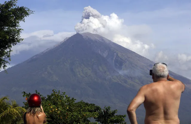 Tourists watch Mount Agung erupt in Karangasem, Bali, Indonesia, Tuesday, July 3, 2018. The volcano on the Indonesian tourist island of Bali erupted Monday evening, ejecting a 2,000-meter-high (6,560-foot-high) column of thick ash and hurling lava down its slopes. (Photo by Firdia Lisnawati/AP Photo)
