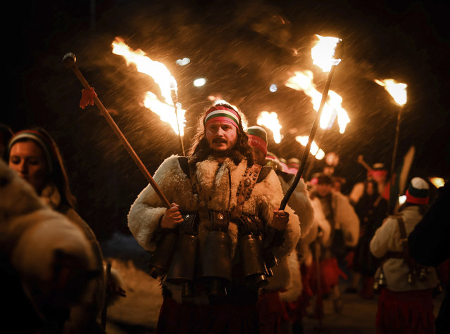Bulgarian kukeri dancers hold their torches as they perform Surva ritual celebrating the New Year with colorful garments, bells and masks, to ward off evil spirits and bring prosperity, in the village of Svetlya, Bulgaria, Monday, late January 13, 2025. (Photo by Valentina Petrova/AP Photo)