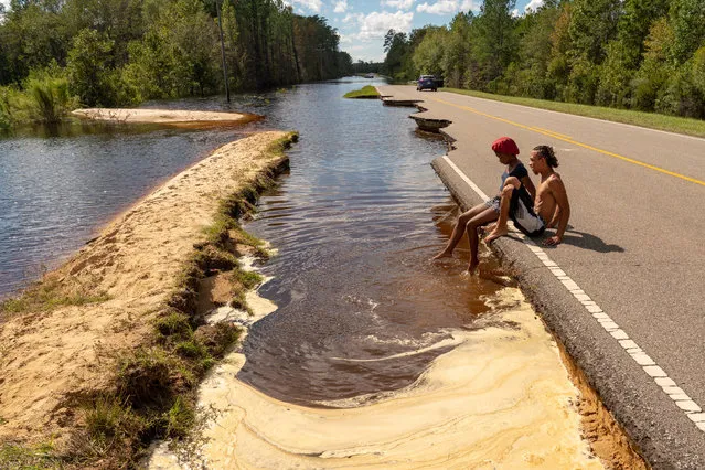 Two young friends cool off in the flood waters by Highway 210 in Currie, North Carolina, US on September 18, 2018 where a section of the road was washed away following Hurricane Florence. (Photo by Ken Cedeno/UPI/Barcroft Images)