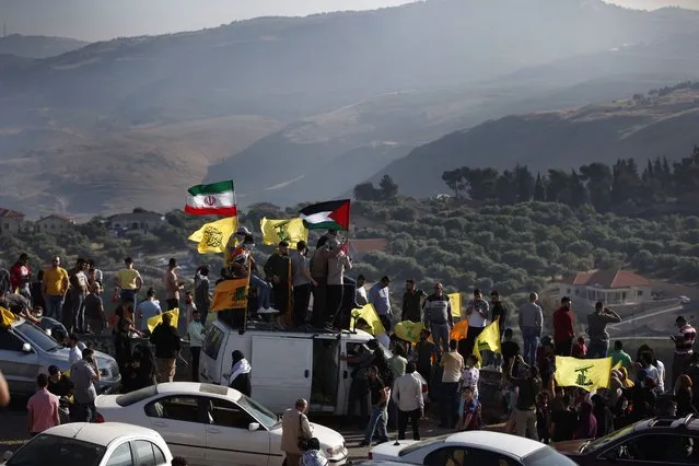 Hezbollah supporters wave their group, Iranian and Palestinian flags, during a protest in solidarity with Palestinians amid an escalating Israeli military campaign in Gaza, on the Lebanese-Israeli border in front of the Israeli settlement of Metula, background, near the southern village of Kafr Kila, Lebanon, Friday, May 14, 2021. (Photo by Mohammed Zaatari/AP Photo)