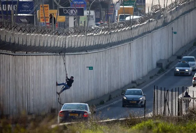 A Palestinian man uses a rope to descend over a section of Israel's controversial separation barrier that separates the West Bank city of al-Ram from east Jerusalem on February 24, 2016. Many Palestinians from the West Bank cross illegally into Israel everyday in search for work. (Photo by Thomas Coex/AFP Photo)