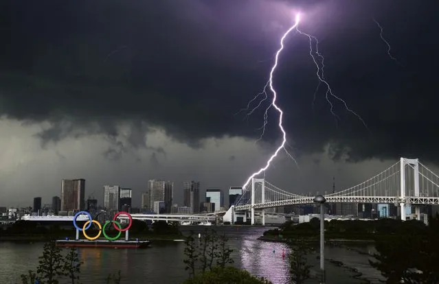 Lightning illuminates the sky over the Olympic rings and the Rainbow Bridge in Tokyo, Sunday, July 11, 2021. The opening ceremony of the postponed 2020 Summer Olympics is scheduled to be held in less than two weeks. (Photo by Kyodo News via AP Photo)