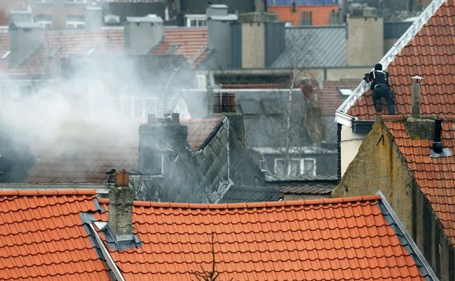 A masked Belgian policeman secures the area from a rooftop above the scene where shots were fired during a police search of a house in the suburb of Forest near Brussels, Belgium, March 15, 2016. Teargas is seen at left. (Photo by Francois Lenoir/Reuters)