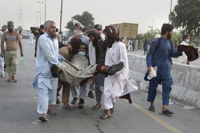 Supporters of Tehreek-e-Labiak Pakistan, a banned radical Islamist party, help their colleague injured in a clash with police during a protest march toward Islamabad, on the outskirts of Lahore, Pakistan, Saturday, October 23, 2021. Thousands of supporters of the banned radical Islamist party Saturday departed the eastern Pakistan city of Lahore, clashing for a second straight day with police who lobbed tear gas into the crowd, a party spokesman and witnesses said. (Photo by K.M. Chaudary/AP Photo)