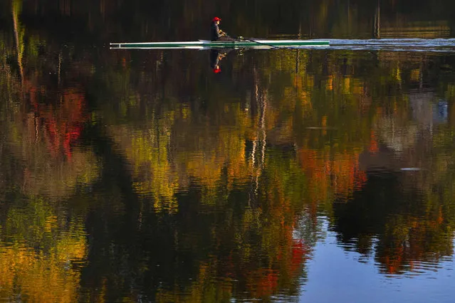 Rower Heather Rankin glides her single scull across placid water reflecting the changing colors of fall foliage on the Androscoggin River, Wednesday, October 6, 2021, in Brunswick, Maine. (Photo by Robert F. Bukaty/AP Photo)