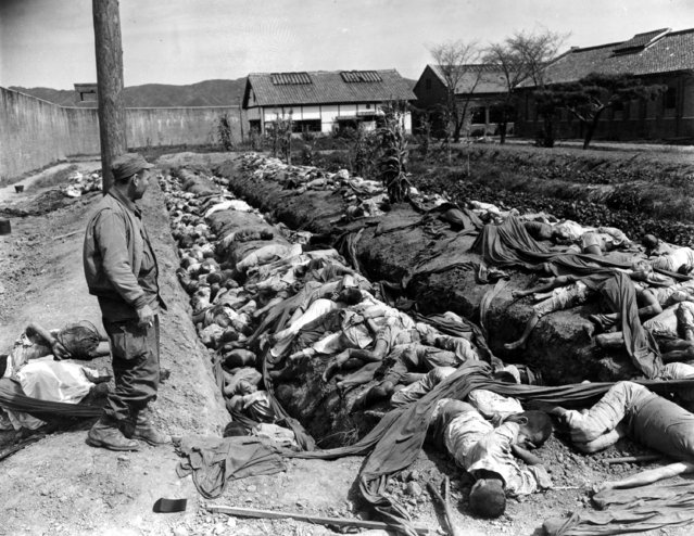 Bodies of some 400 Korean civilians lie in and around trenches in Taejon's prison yard during the Korean War, September 28, 1950.  The victims were bound and slain by retreating Communist forces before the 24th U.S. Division troops recaptured the city Sept. 28.  Witnesses said that the prisoners were forced to dig their own trench graves before the slaughter.  Looking on, at left, is Gordon Gammack, war correspondent of the Des Moines Register and Tribune. (Photo by James Pringle/AP Photo)