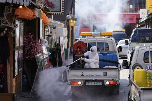 A local district health official in protective gear disinfects shop fronts as a precaution against the coronavirus in Seoul, South Korea, Friday, October 29, 2021. South Korea has allowed larger social gatherings and lifted business-hour restrictions on restaurants starting Monday, Nov. 1, 2021, in what officials describe as the first step of an attempt to restore some pre-pandemic normalcy. (Photo by Lee Jin-man/AP Photo/File)
