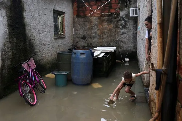A child catches a flip flop outside a house surrounded by flood waters after heavy rains in Duque de Caxias, Rio de Janeiro state, Brazil on March 24, 2024. (Photo by Pilar Olivares/Reuters)