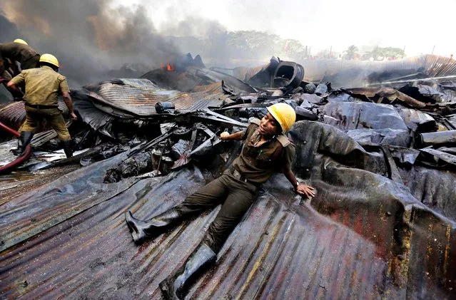 An exhausted firefighter rests on debris as they battle to extinguish a huge fire in a paint factory in Howrah, 30 km west of Calcutta, Eastern India, 12 March 2014. A major fire broke out at a factory of Shalimar Paints Limited in Howrah early morning. According to police and media reports, 25 fire engines fought for close to six hours to extinguish the blaze. Noboby was injured. (Photo by Piyal Adhikary/EPA)