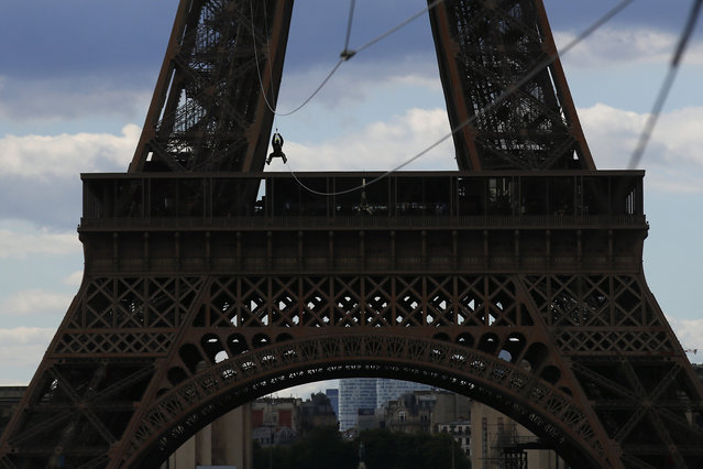 A participant rides a zipline tied from the second floor of the Eiffel Tower, 115 metres above the Champ de Mars gardens along an 800-meters long cable, as part of a free event in Paris, France, Tuesday, May 28, 2019. (Photo by Francois Mori/AP Photo)