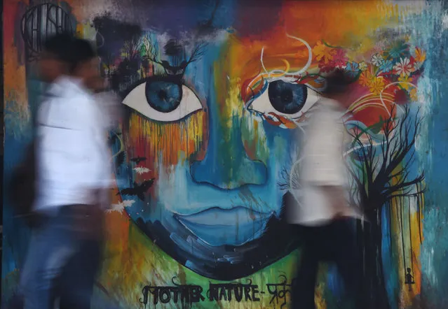Indian officegoers walk past a wall displaying a mural in Mumbai on April 3, 2017. Graffiti featuring as social awareness messages, civic causes, religious figures, politicians, as well as daily life scenes cover the walls of certain streets of Mumbai. Written in English, Hindi or Marathi, these messages are of late being used for educational purposes than merely contributing to embellish the country's financial capital. (Photo by Indranil Mukherjee/AFP Photo)