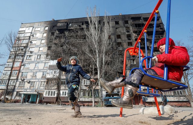 Children play in front of a building damaged in fighting during Ukraine-Russia conflict, in the besieged southern port of Mariupol, Ukraine on March 23, 2022. (Photo by Alexander Ermochenko/Reuters)