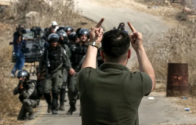 A Palestinian protester gives the middle finger gesture with both of his hands towards Israeli border guards amidst clashes during a demonstration against construction on an Israeli outpost near the Palestinian village of Turmus Ayya and the Israeli settlement of Shilo, north of Ramallah in the occupied West Bank, on October 17, 2019. (Photo by Jaafar Ashtiyeh/AFP Photo)