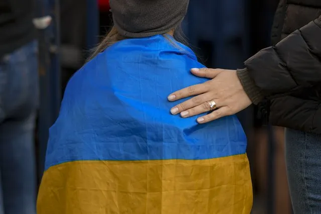 A woman puts her hand on the back of a child draped in the Ukrainian flag during a protest against Russia's war in Ukraine, in front of the Russian embassy in Bucharest, Romania, Sunday, March 27, 2022. (Photo by Andreea Alexandru/AP Photo)