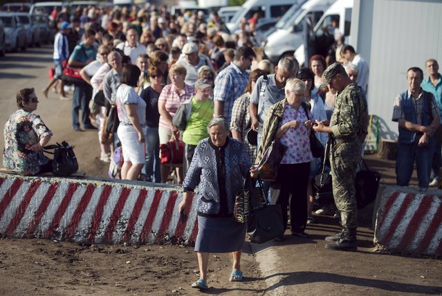 People stand in a line to pass through the checkpoint “Zaitsevo”, demarcating territories controlled by the Ukrainian armed forces and the forces of the self-proclaimed Donetsk People's Republic, near Artemivsk, Donetsk region, July 17, 2015. (Photo by Maksim Levin/Reuters)