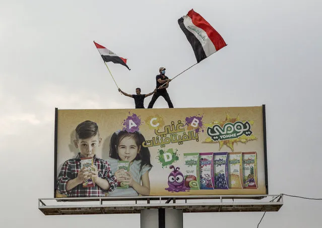 Iraqi protesters wave national flags as they stand atop a billboard during an anti-government demonstration outside the local government headquarters in the southern city of Basra on October 25, 2019. More than a dozen demonstrators died in renewed rallies across Iraq's capital and the south, with the first reported use of live rounds in this wave of protests. (Photo by AFP Photo/Stringer)