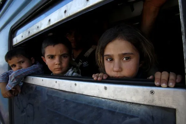 In this photo taken on Thursday, July 23, 2015 children, migrants from Afghanistan, look through a window after boarding a train to Serbia with their parents, at the railway station in the southern Macedonian town of Gevgelija. (Photo by Boris Grdanoski/AP Photo)
