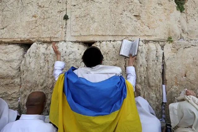 A Jewish worshipper drapped in a Ukranian flag, takes part in the Cohanim prayer (priest's blessing) during the Passover holiday at the Western Wall in Jerusalem's Old City on April 18, 2022. (Photo by Gil Cohen-Magen/AFP Photo)