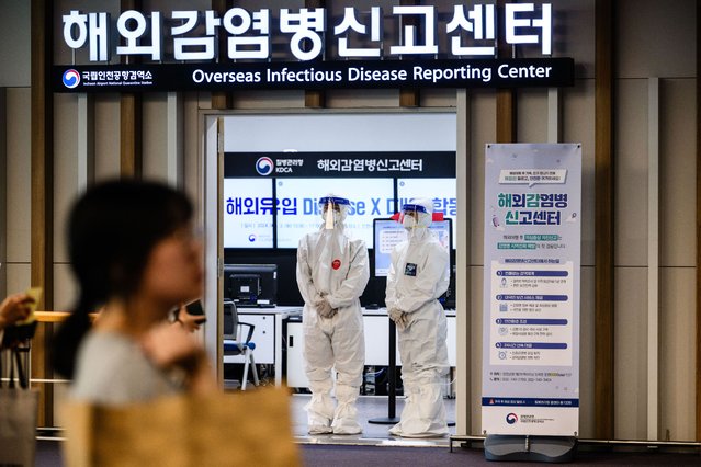 A passenger walks past airport staff members (C) standing in a doorway of the Overseas Infectious Disease Reporting Centre at the Incheon International Airport Terminal 2 on September 3, 2024, on the sidelines of a training drill to check the quarantine response system in the event of suspected patients and to facilitate cooperation systems among related organisations in preparation for the influx of new infectious diseases. (Photo by Anthony Wallace/AFP Photo)