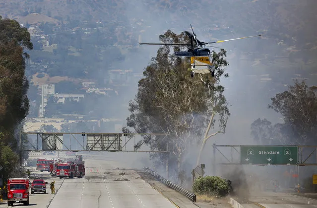 Firefighters use a helicopter to douse a fire near California State Route 2 after a brush fire swept through threatening homes in Los Angeles on Sunday, June 19, 2016. Los Angeles firefighters say they have contained the fire in the densely populated neighborhood along a freeway. (Photo by Damian Dovarganes/AP Photo)