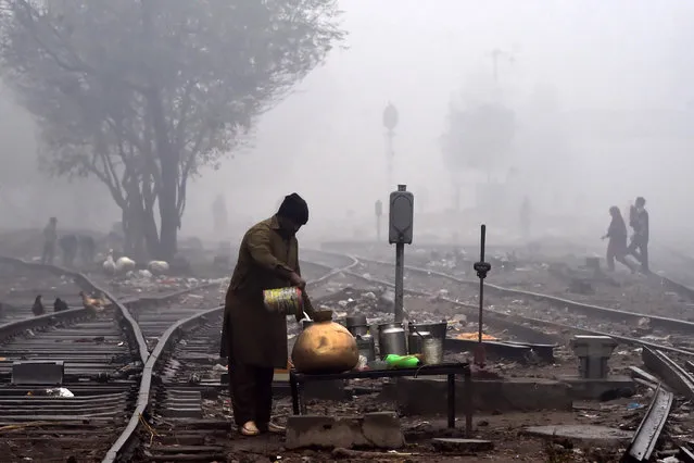 A milkman fills a pot with milk on a railway track during a cold and foggy morning in Lahore, Punjab Province on January 8, 2020. (Photo by Arif Ali/AFP Photo)