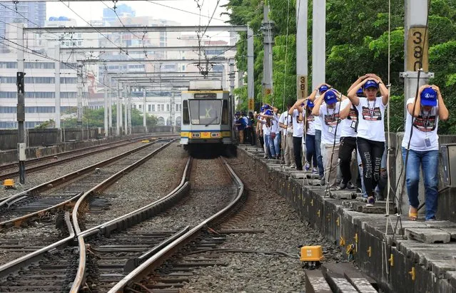 Light Rail Transit (LRT) mock passengers use their hands to cover their heads as they pass through a walkway beside the train tracks during a metrowide simultaneous earthquake drill in metro Manila, Philippines June 22, 2016. (Photo by Romeo Ranoco/Reuters)