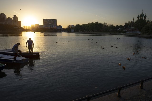 Workers prepare a boat during sunset with a temperature of 24°C (75.2 F) on the Great Palace Pond with the Church of the Holy Trinity in Ostankino in the background in Moscow, Russia, Wednesday, September 25, 2024. (Photo by Alexander Zemlianichenko/AP Photo)