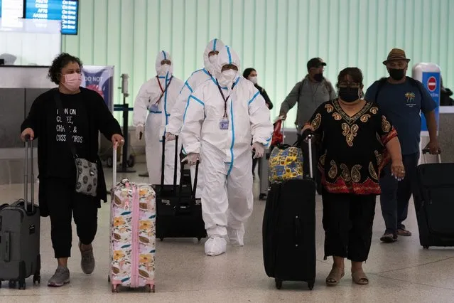 Air China flight crew members in hazmat suits walk through the arrivals area at Los Angeles International Airport in Los Angeles, Tuesday, November 30, 2021. Brazil and Japan joined the rapidly widening circle of countries to report cases of the omicron variant of the coronavirus on Tuesday. (Photo by Jae C. Hong/AP Photo)