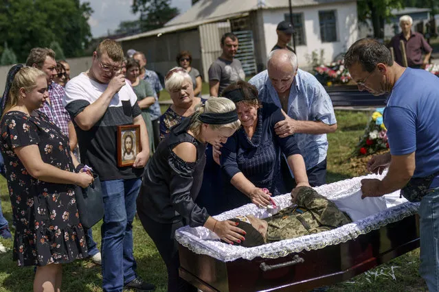 Lilia Panchenko is pulled away by her husband, Anatolii, right, as she says her final goodbye to their son, Oleh, along with his daughter, Ruslana, left, before his casket is covered during his burial service in Pokrovsk, Donetsk region, eastern Ukraine, Thursday, August 4, 2022. Ukrainian soldier Oleh Panchenko, 48, was killed July 27 by Russian forces fighting in the Donetsk region. (Photo by David Goldman/AP Photo)
