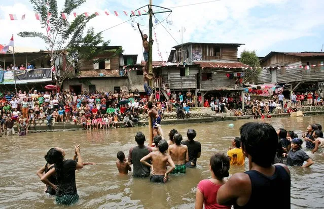 Indonesian youths struggle to reach the prizes hanging at the top of a greased-pole during a greased-pole climbing competition held in a river to celebrate the country's Independence Day in Medan, North Sumatra, Indonesia, Sunday, August 17, 2014. (Photo by Dita Alangkara/AP Photo)