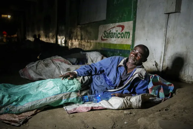 In this photo taken Tuesday, March 24, 2020, a homeless person prepares to sleep next to others on the side of a road in the Mathare slum, or informal settlement, of Nairobi, Kenya. Many slum residents say staying at home or social-distancing is impossible for those who live hand to mouth, receiving daily wages for informal work with no food or economic assistance from the government, as is maintaining sanitation where a pit latrine can be shared by over 50 people. The new coronavirus causes mild or moderate symptoms for most people, but for some, especially older adults and people with existing health problems, it can cause more severe illness or death. (Photo by Brian Inganga/AP Photo)