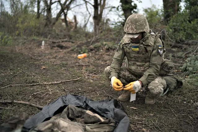 A Ukrainian serviceman identifies the body of a Ukrainian soldier in a retaken area near the border with Russia in Kharkiv region, Ukraine, Saturday, September 17, 2022. (Photo by Leo Correa/AP Photo)