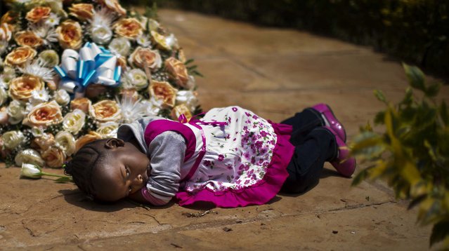 Nicole Tashly, 2, lies quietly on the ground holding the white rose her mother Esther Muthoni, left, instructed her to lay at the memorial monument while they remember her father Paul Muriithi Muriuki who died in the Westgate Mall attack, as they and other families of the victims lay flowers and remember, at the Amani Garden memorial site in the Karura Forest in Nairobi, Kenya Sunday, September 21, 2014. (Photo by Ben Curtis/AP Photo)