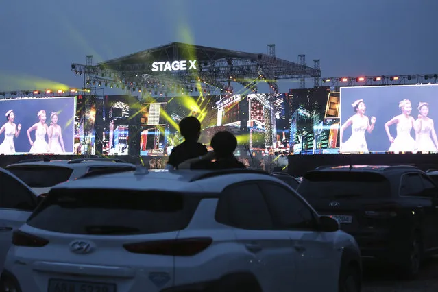 People in their car watch the Stage X drive-in concert at KINTEX parking lot in Goyang, South Korea, Saturday, May 23, 2020. The concert's aim is to provide entertainment for South Korean citizens who have been craving for music events that have been suspended during the coronavirus outbreak. (Photo by Ahn Young-joo/AP Photo)