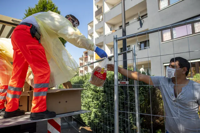 Red Cross helpers wear face masks and protective clothing while distributing bread to residents of a house that has been quarantined in Verl, Germany, Sunday, June 21, 2020. The city of Verl has set up a quarantine after positive corona tests on numerous employees of the Toennies slaughterhouse living in several apartment buildings in the Suerenheide district. (Photo by David Inderlied/dpa via AP Photo)