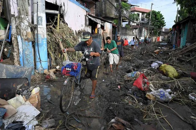 Men carrying their bicyclea as they walk along a debris-covered street in Noveleta, Cavite on October 30, 2022, a day after Tropical Storm Nalgae hit. Emergency workers scrambled to rescue residents trapped by floods in and around the Philippine capital on October 30 as Tropical Storm Nalgae swept out of the country after killing at least 48 people. (Photo by Jam Sta Rosa/AFP Photo)