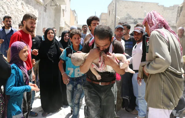 A Syrian man holds the body of his child after it was taken from under the rubble of destroyed buildings following a reported air strike on the rebel-held neighbourhood of al-Marjah in the northern city of Aleppo, on July 24, 2016. (Photo by Ameer Alhalbi/AFP Photo)