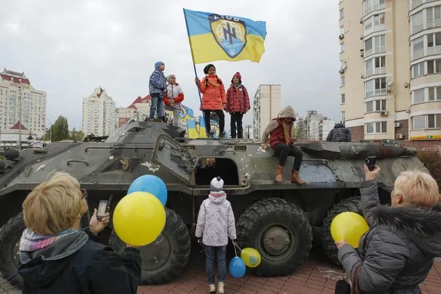 People gathered around a damaged armoured personnel carrier (APC) in Kiev October 21, 2014. The APC is one of a number of vehicles captured by members of the Ukrainian interior ministry's “Azov” battalion, according to their commander, from pro-russian separatists in Eastern Ukraine. (Photo by Valentyn Ogirenko/Reuters)