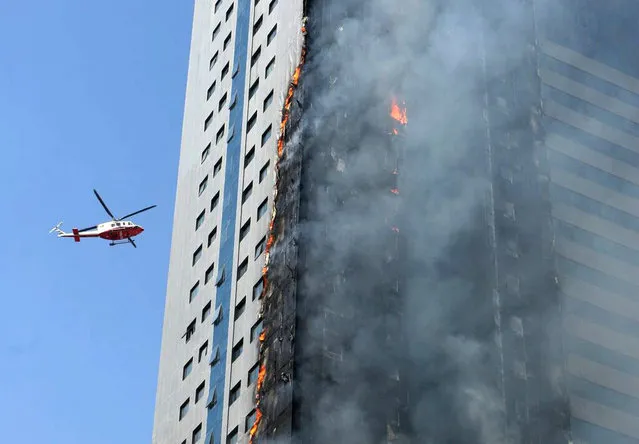 A helicopter hovers over a skyscraper which caught fire in Sharjah, United Arab Emirates, Thursday, October 1, 2015. It was not immediately clear if there were any casualties. The Sharjah civil defense directorate had no immediate comment. (Photo by AP Photo)