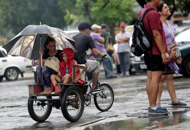 A woman and her son take a bicycle taxi through Havana during rain, August 30, 2016. (Photo by Enrique de la Osa/Reuters)