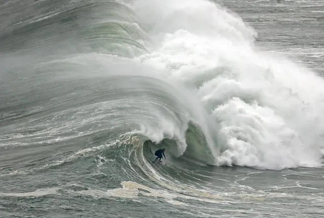 A surfer rides a wave during a tow-in surfing session at the Praia do Norte or North beach, in Nazare, Portugal, Thursday, November 20, 2014. (Photo by Francisco Seco/AP Photo)