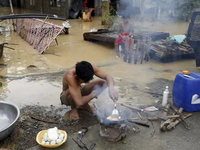 A typhoon victim cooks eggs in front of their house, partially submerged in floodwaters, in Jaen, Nueva Ecija in northern Philippines October 20, 2015, after the province was hit by Typhoon Koppu. (Photo by Erik De Castro/Reuters)