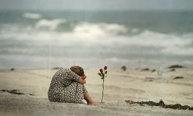 Sitting near a rose she placed in the sand at Smith Point beach in Fire Island, N.Y. , a woman mourns the loss of some of her friends Friday July 26, 1996, who were part of the TWA flight 800 flight crew. The Navy is still searching for victims and parts of the plane. (Photo by Mark Lennihan/AP Photo)