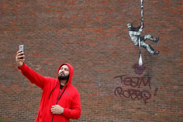 A man takes a selfie with a vandalised mural by artist Banksy on a wall at HM Reading Prison, in Reading, Britain on March 16, 2021. (Photo by Paul Childs/Reuters)