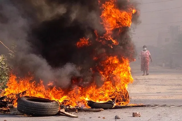 This photo taken and received courtesy of an anonymous source via Facebook on March 22, 2021 shows a woman walking near burning barricades during a crackdown by security forces on demonstrations by protesters against the military coup in Mandalay. (Photo by Handout/FACEBOOK via AFP Photo)
