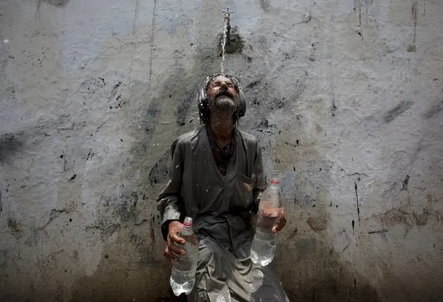 A man cools off from a public tap after filling bottles during intense hot weather in Karachi, Pakistan, June 23, 2015. (Photo by Akhtar Soomro/Reuters)