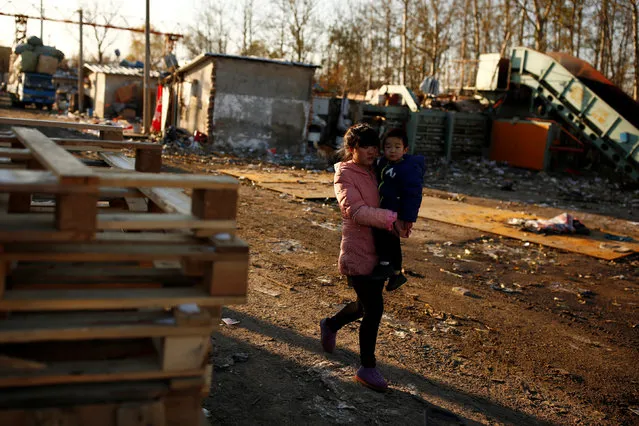 A woman carries a child past a section of a recycling yard that was cleared after authorities closed access for deliveries to instigate the closing down of the facility at the edge of Beijing, China, November 22, 2016. (Photo by Thomas Peter/Reuters)
