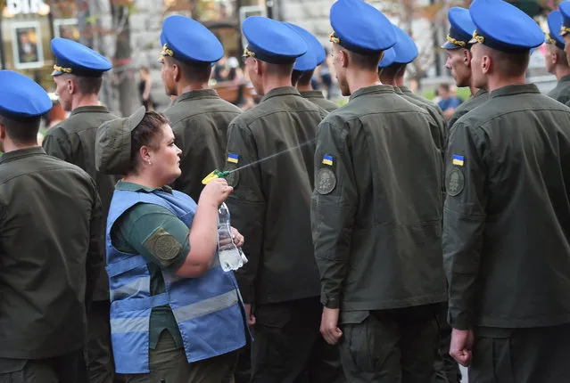 A military nurse sprays Ukrainain servicemen with water cool them down from the heat during a parade rehearsal in the centre of Kiev on August 20, 2018, ahead of Ukraine's Independance Day celebrations on August 24. 4,500 servicemen and 250 pieces of military equipment, including the newest ones produced in Ukraine, will participate in the parade. (Photo by Sergei Supinsky/AFP Photo)