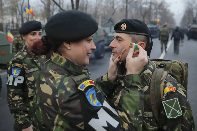 A Romanian military policewoman paints the colors of the Romanian flag on the cheek of a colleague before the National Day parade in Bucharest, Romania, Thursday, December 1, 2016. (Photo by Vadim Ghirda/AP Photo)